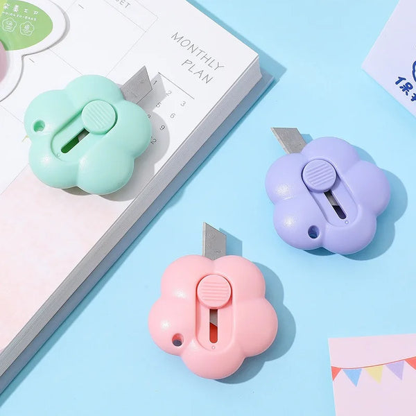 A set of three plastic floral design letter openers and paper cutters in mint green, lavender, and pink on a light blue backg