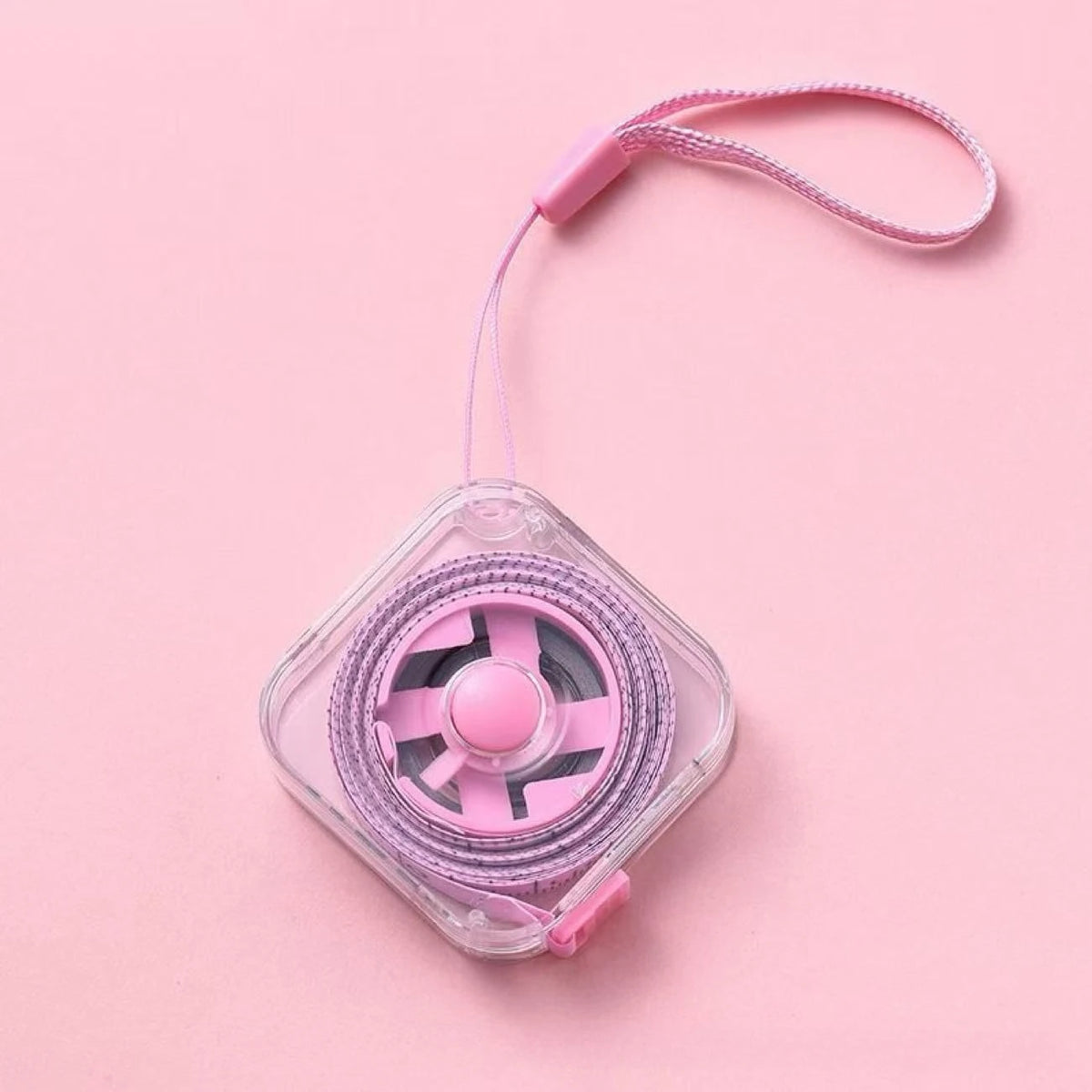 A pink compact retractable measuring tape with a lock is shown against a light pink background.
