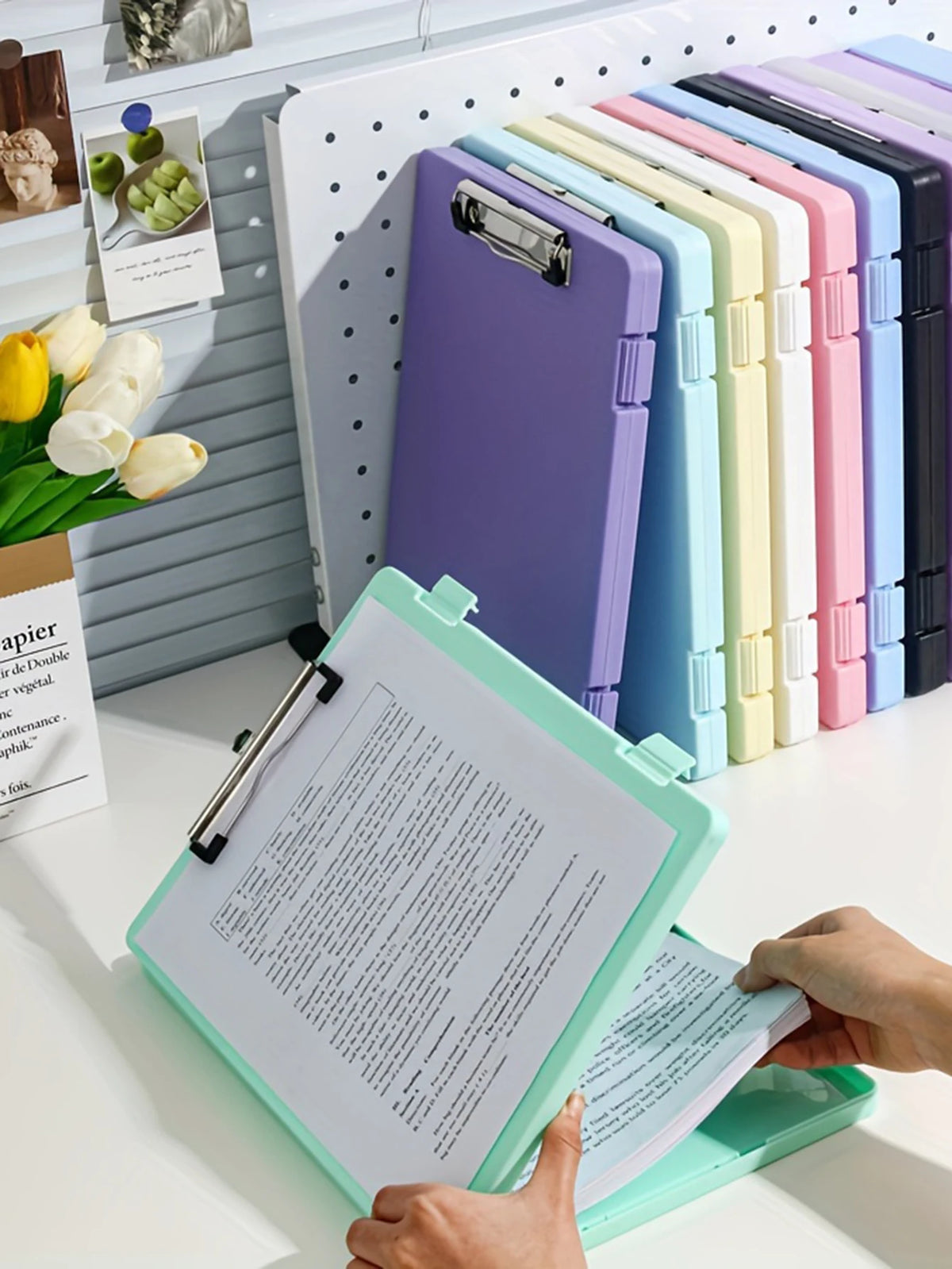 A hand holds an open A4 document and photo storage file box next to a row of colorful file boxes.