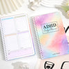 A pink and purple ADHD Daily Planner notebook with a task organizer and lined pages is shown on a white surface.