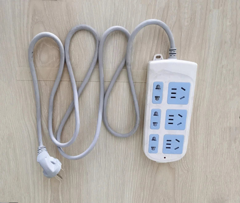 A white extra strong double-sided nano tape dispenser with coiled gray tape and a power cord lying on a light wood surface.