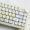 A close-up view of a light beige mechanical keyboard with white keycaps and a gold patterned surface.