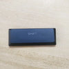 A black rectangular keycap labeled SHIFT resting on a light wooden surface.