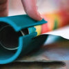 A hand is operating a teal portable mini paper cutting machine to cut paper.