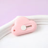 A pink portable utility knife with a heart-shaped body and a circular blade is shown on a white surface.