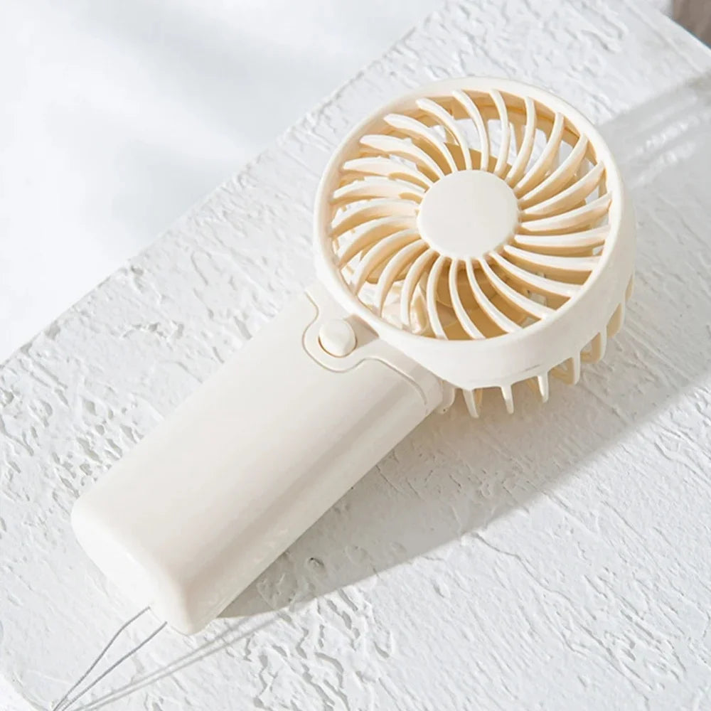 A white portable rechargeable mini handheld fan with a circular grille and a cord resting on a white surface.