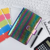 Un set de cahier et de stylo coloré avec des paillettes posé sur un bureau blanc à côté du clavier d'un ordinateur portable.