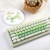 A close-up of a light green mechanical keyboard featuring colorful PBT keycaps and a small set of matching keycaps.