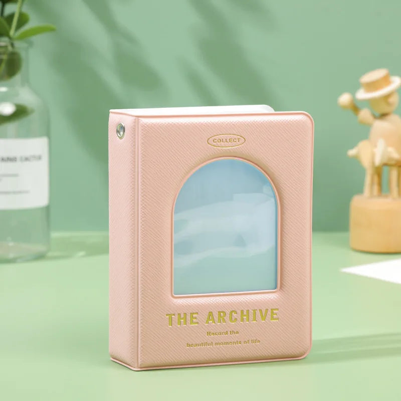 A pink hollow photo card binder labeled The Archive with a translucent cover resting on a green surface.