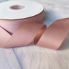 Roll of matte finish satin ribbon in dusty rose color with a portion unwrapped on a light surface.