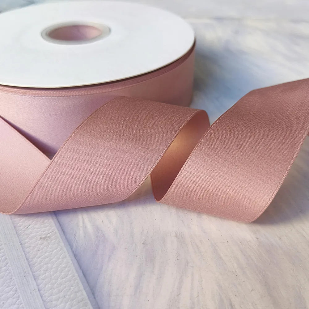 Roll of matte finish satin ribbon in dusty rose color with a portion unwrapped on a light surface.