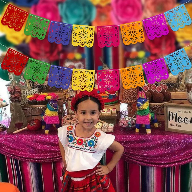 A young girl smiling in front of a colorful papel picado banner decoration.