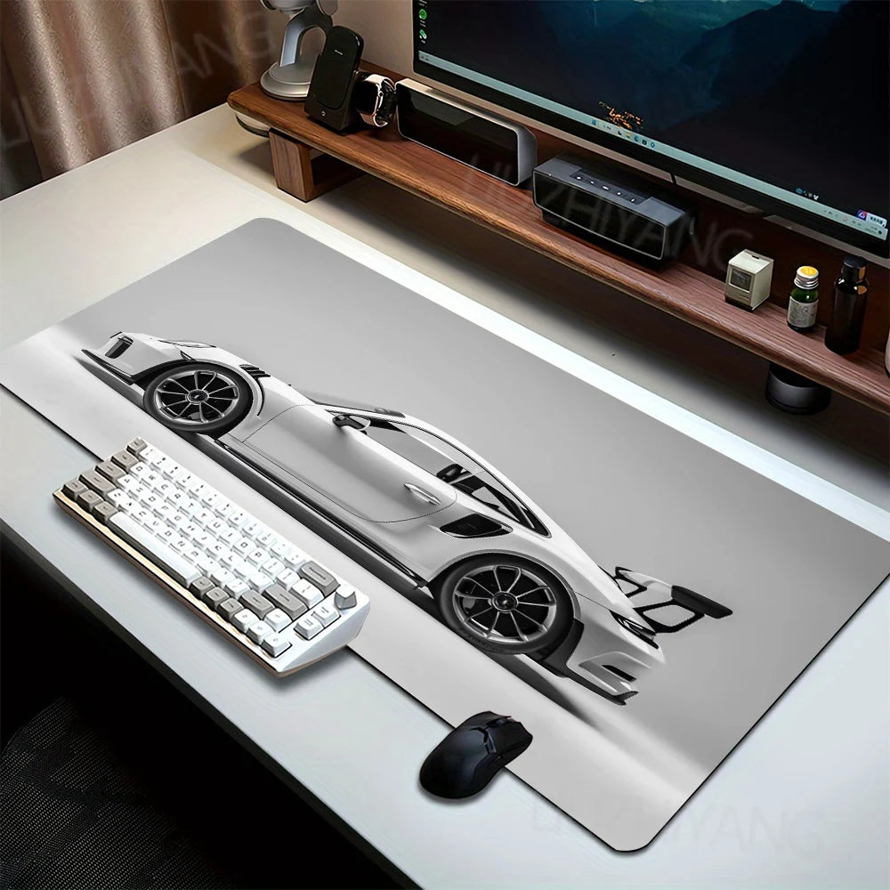 A large sports car pattern gaming mousepad displayed on a wooden desk with a keyboard and mouse visible.