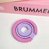 A pink and purple magnetic phone grip and stand with a foldable ring resting on a white surface.