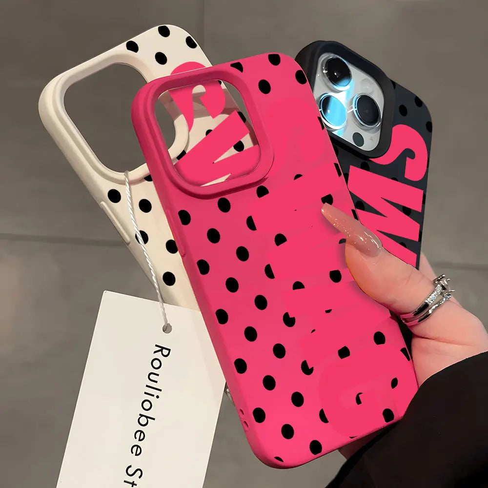 A hand holds a bright pink polka dot phone case and a black case with white lettering.