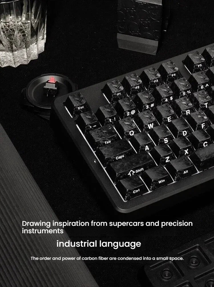 Close-up of black carbon fiber texture keycaps resting on a mechanical keyboard with surrounding tools and dark surface.