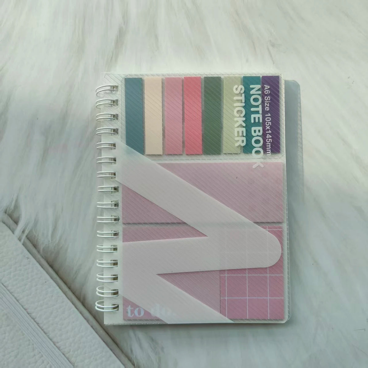 A stack of pastel colored A6 sticky note notebook with a pink and white design on a white fluffy surface.