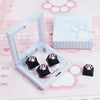 A white plastic case containing black cat claw keycaps and a box labeled Cat Claw Keycaps for MX Switches on a pink backgroun