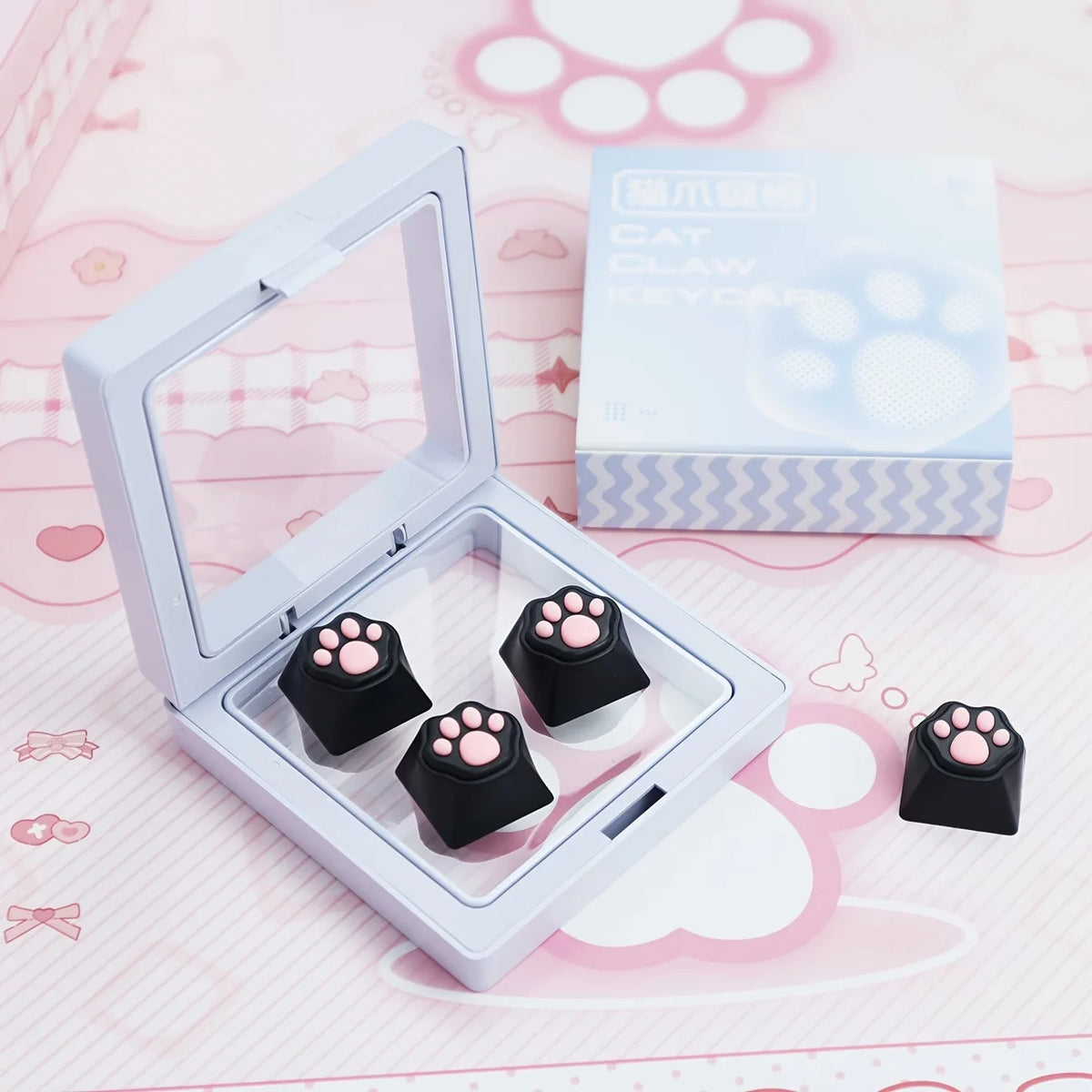 A white plastic case containing black cat claw keycaps and a box labeled Cat Claw Keycaps for MX Switches on a pink backgroun