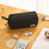 A black multi-layer stationery storage pencil case rests on a wooden table next to a ruler and a calculator.