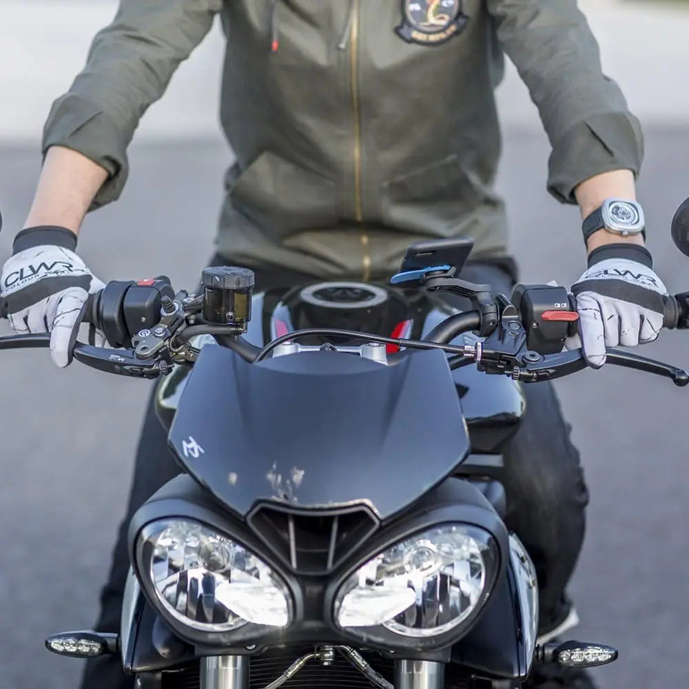 A person is holding a black motorcycle with a phone mount attached to the handlebars.