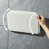 A hand is shown folding a white, rectangular wall shelf for no-drill storage onto a gray tiled surface.