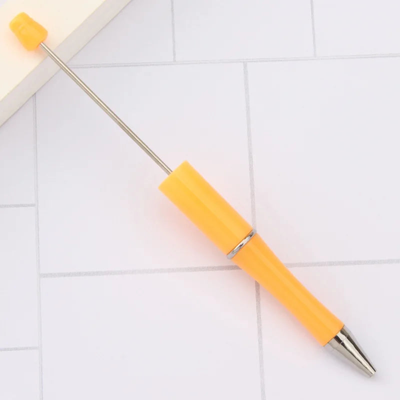 A yellow DIY beadable pen with a silver clip and a gold-tipped needle is shown on a white surface.
