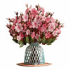 A bouquet of pink cherry blossoms arranged in a light blue ceramic vase on a wooden coaster.