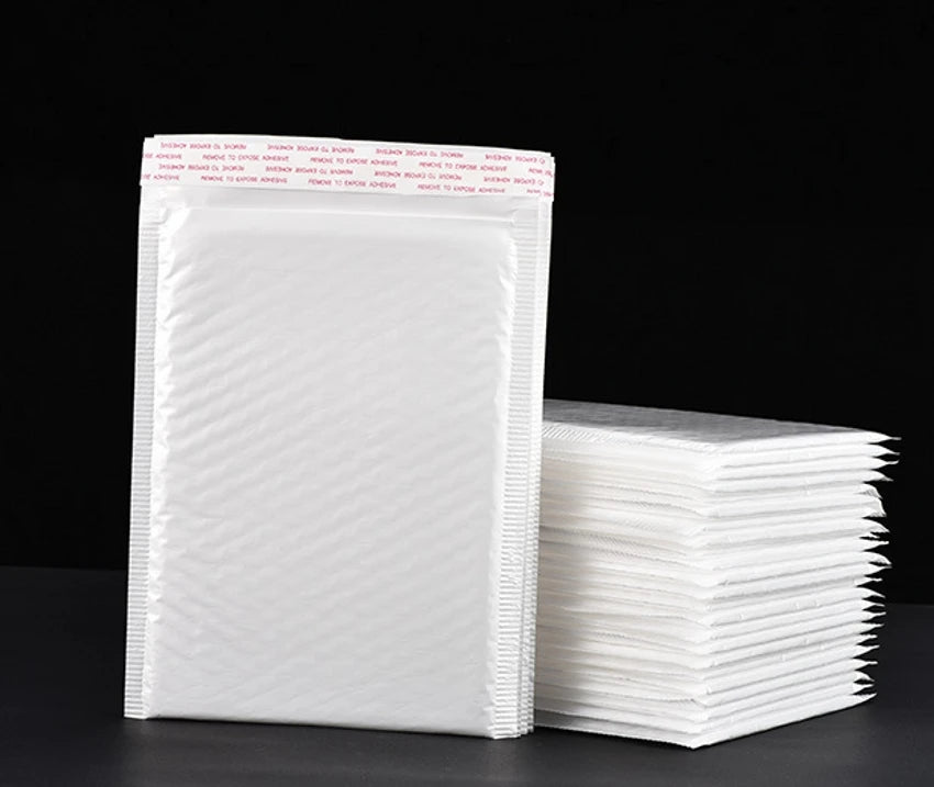 A stack of white self-sealing pearl film bubble shipping bags is shown on a dark surface.