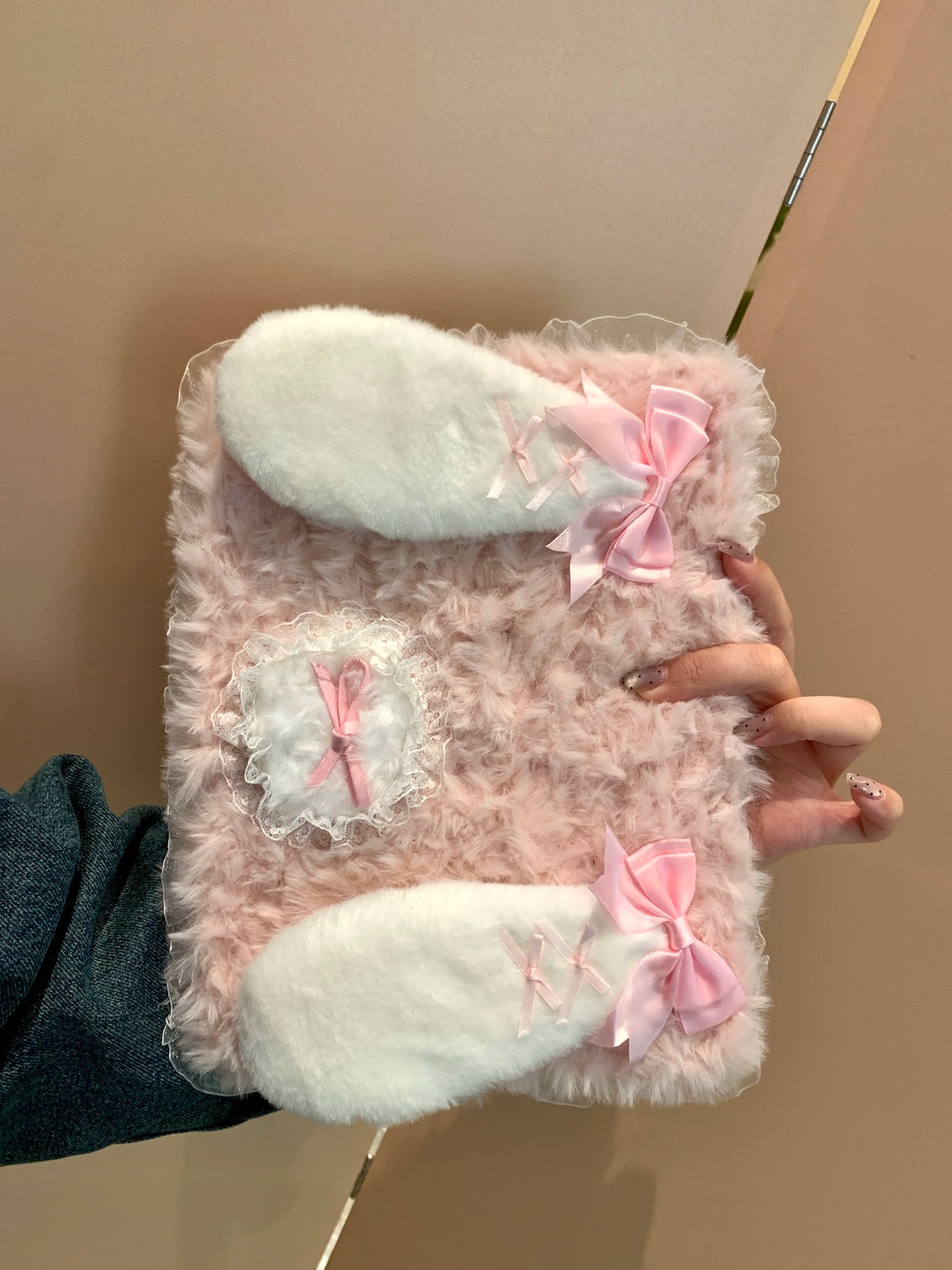 A pink fluffy rabbit plush case with white ears is held by a hand against a light background.