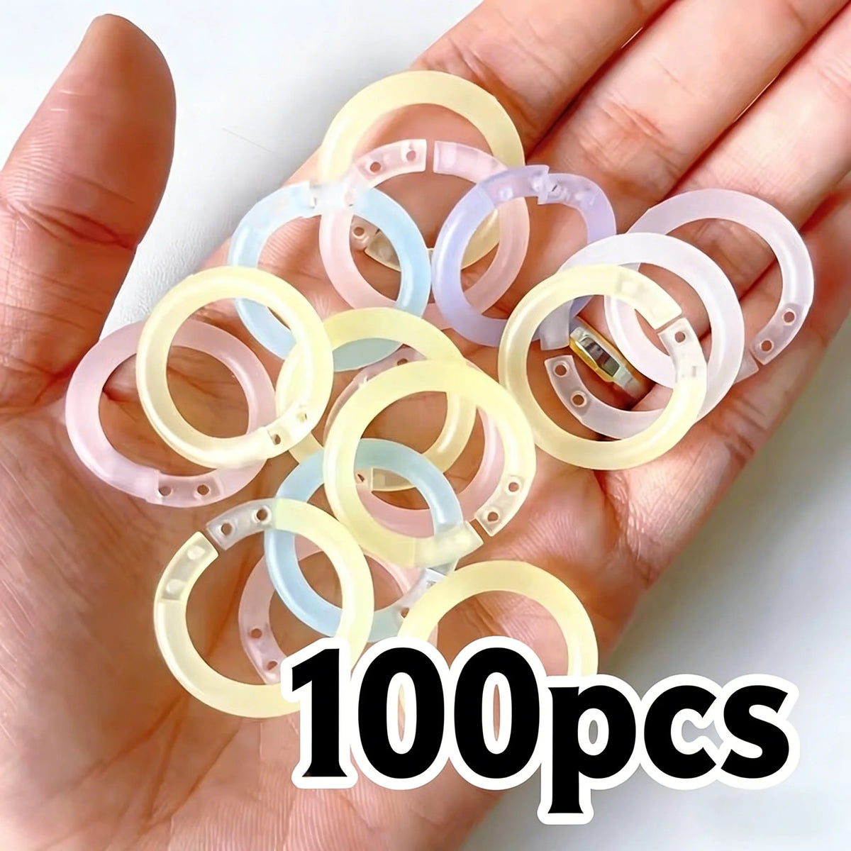 A hand holds a collection of 100 reusable plastic binding rings in various pastel colors like pink, yellow, and blue.