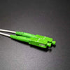 A close-up of a green single-mode fiber optic cable connector with a white jacket and silver tip.