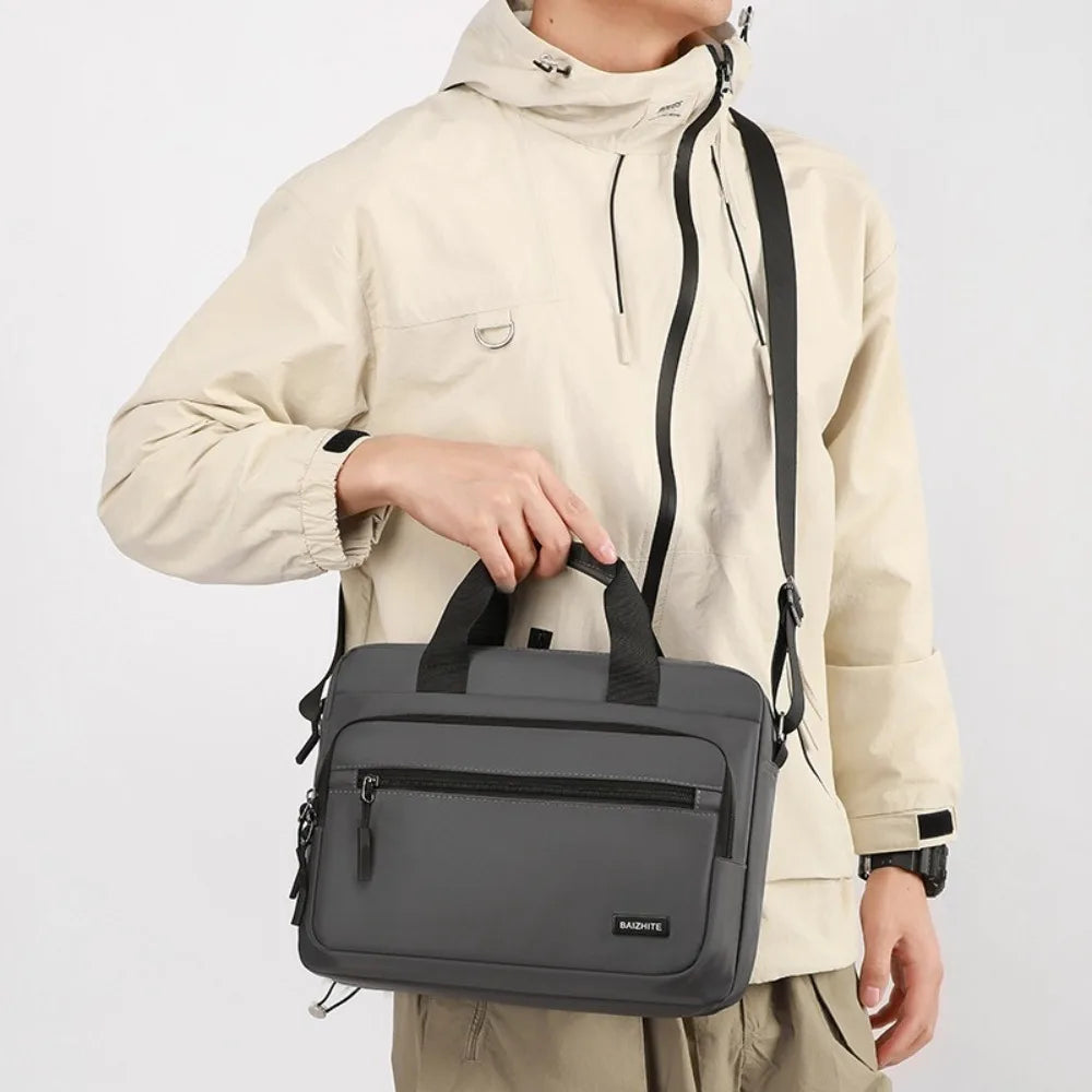 A man wearing a beige hoodie holds a dark gray Oxford cloth crossbody briefcase with a laptop compartment.