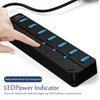 A hand is pressing a button on a black 7-port USB hub with LED indicators to power on the interface.
