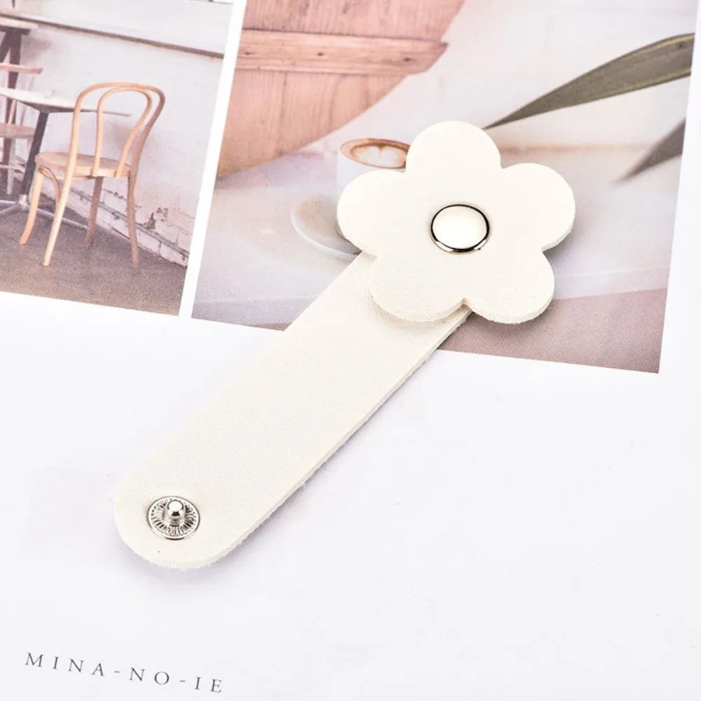 A beige leather flower cable organizer with a loop and a metal clasp is shown on a white background.
