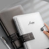 Un carnet à feuilles détachées transparent argenté avec une couverture noire et un stylo noir à côté.