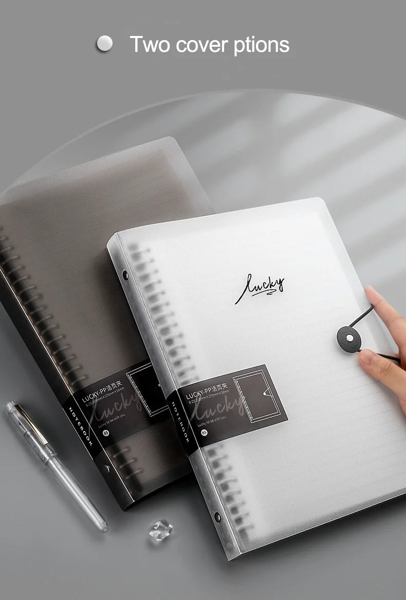 Un carnet à feuilles détachées transparent argenté avec une couverture noire et un stylo noir à côté.