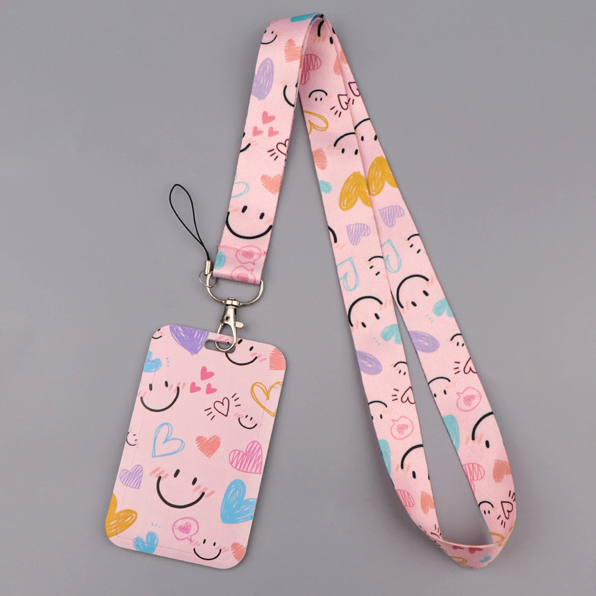 A pink heart-shaped lanyard with a repeating pattern of cute faces and hearts
