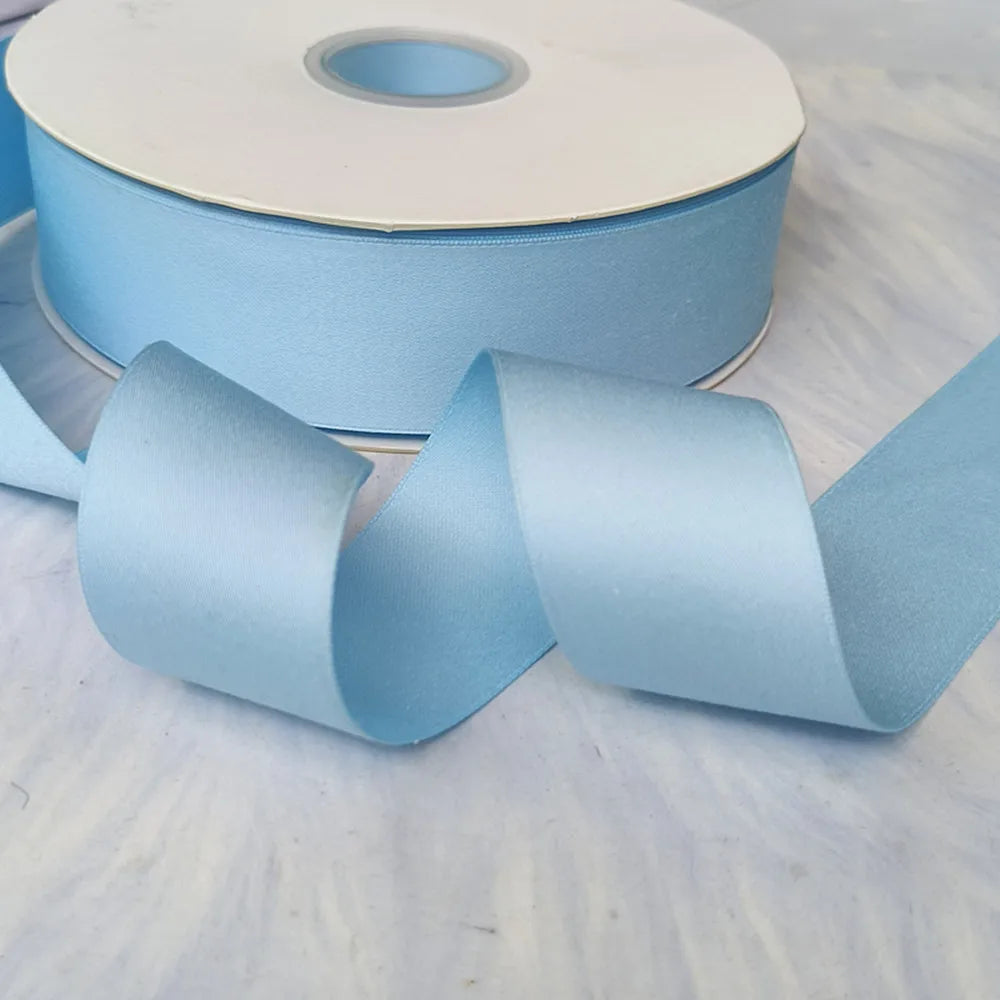 A roll of light blue matte finish satin ribbon with a visible core and several unwound strips lying on a white surface.
