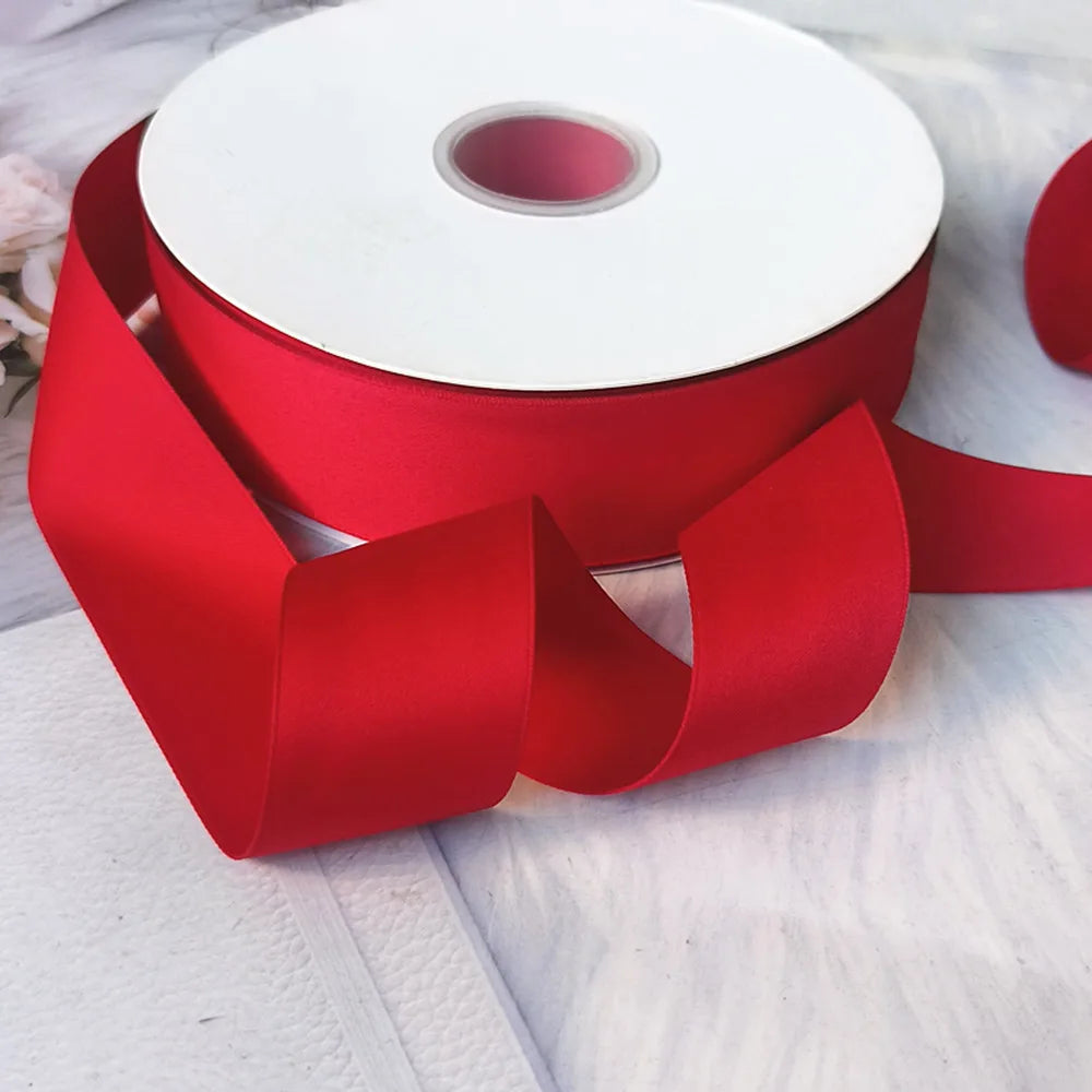 A roll of red matte finish satin ribbon for crafts and decor lying on a white surface.