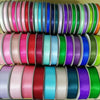 Ein Stapel doppelseitiger Satinbandrollen in verschiedenen Rosa-, Blau-, Grün- und Violetttönen.
