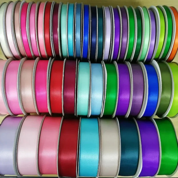 Ein Stapel doppelseitiger Satinbandrollen in verschiedenen Rosa-, Blau-, Grün- und Violetttönen.