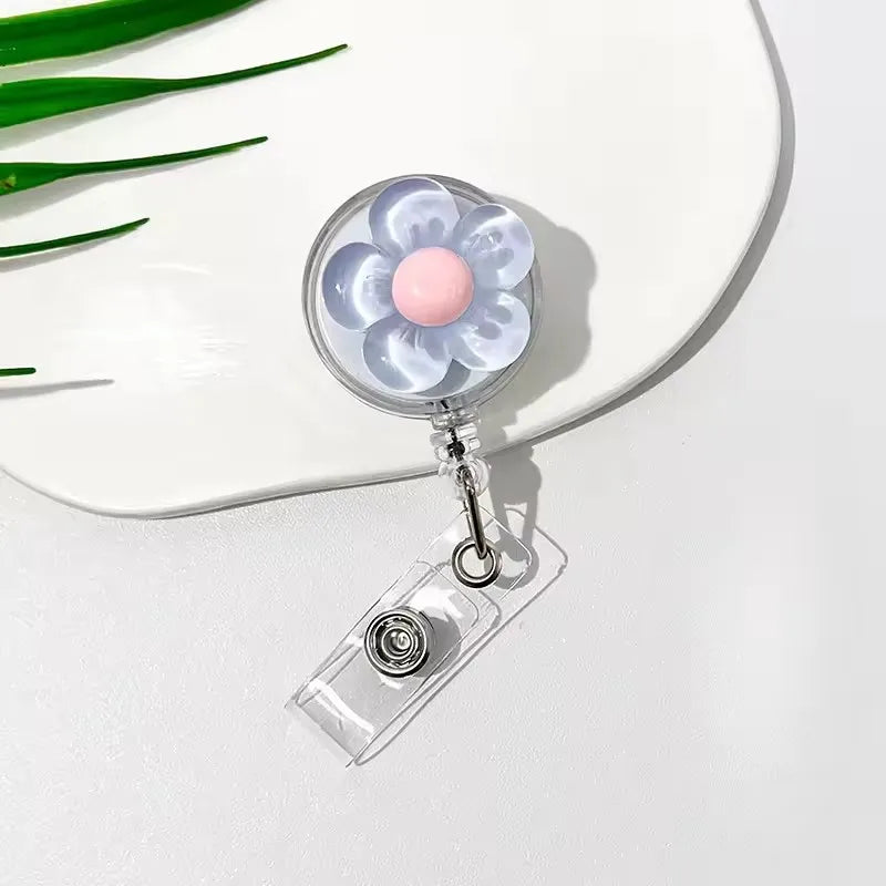 A clear plastic retractable ID badge holder with a floral pull buckle featuring light purple and pink accents.