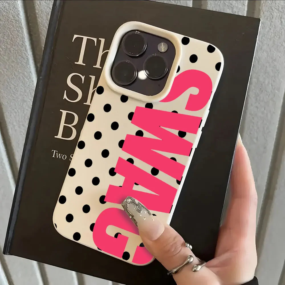 A pink polka dot phone case with a clear back and white lettering is shown on a black box.