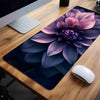 A dark purple and pink floral design mouse pad placed on a wooden desk next to a computer monitor.