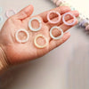 A hand holds several colorful reusable plastic binding rings of varying shades including pink, white, and yellow.