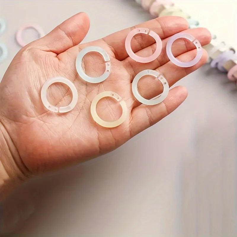 A hand holds several colorful reusable plastic binding rings of varying shades including pink, white, and yellow.