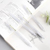 A set of minimalist mechanical pencils in clear plastic and gold accents resting on a white page with handwritten text.