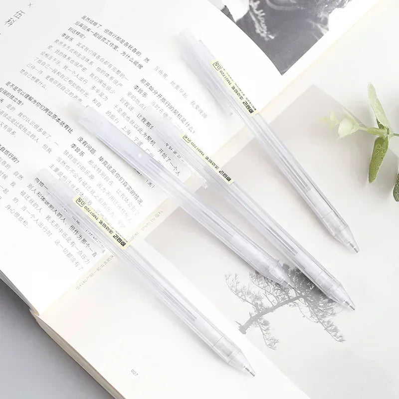 A set of minimalist mechanical pencils in clear plastic and gold accents resting on a white page with handwritten text.