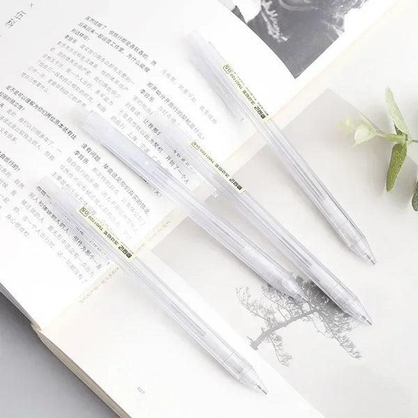 A set of minimalist mechanical pencils in clear plastic and gold accents resting on a white page with handwritten text.